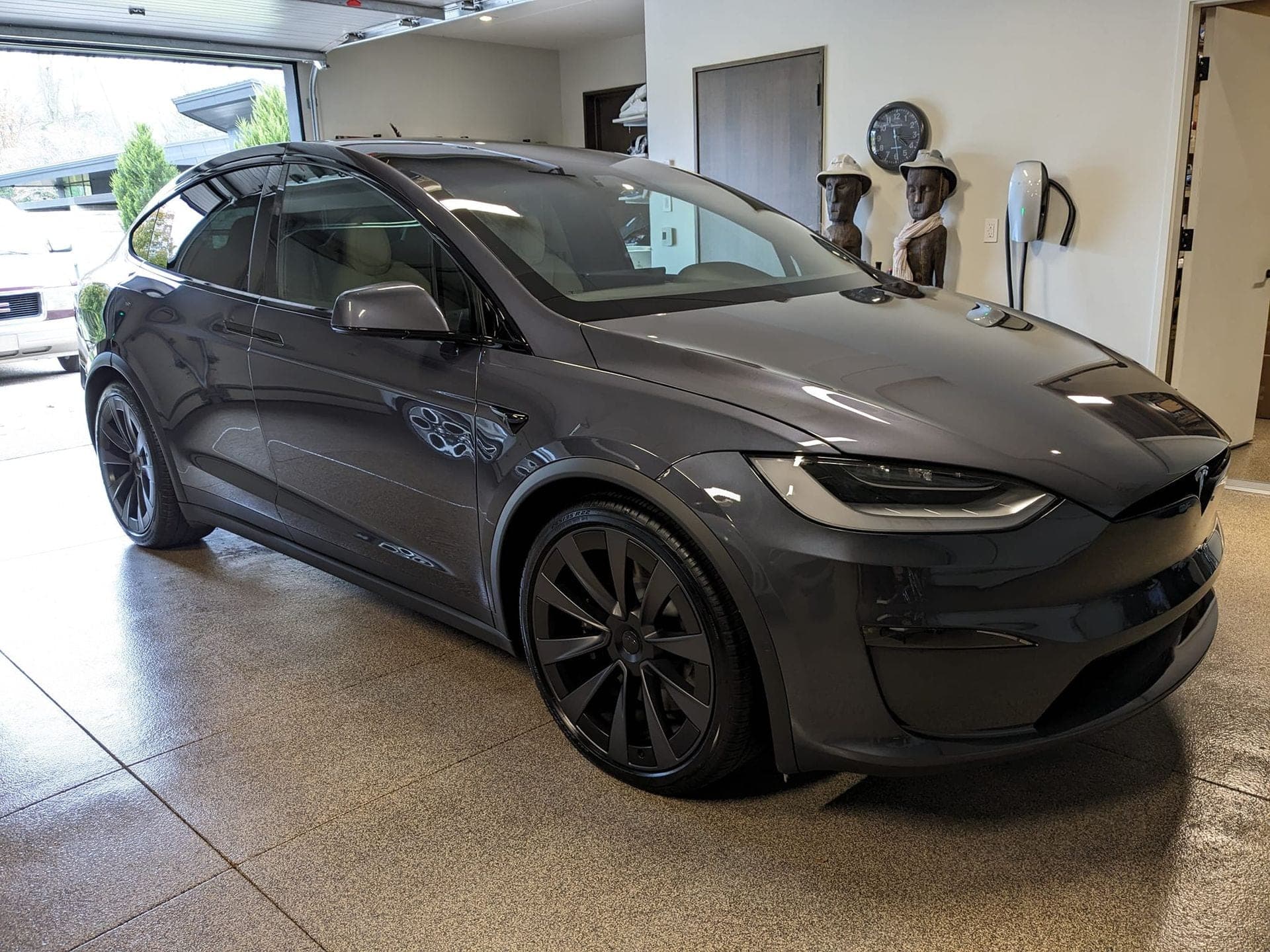 A dark gray Tesla Model X parked inside a garage with speckled flooring.